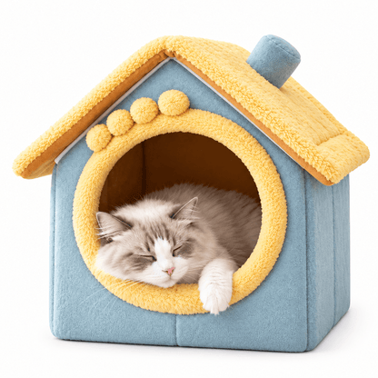 Yellow roof and blue plush cat house bed with pom-pom trim and a fluffy cat napping in the doorway.