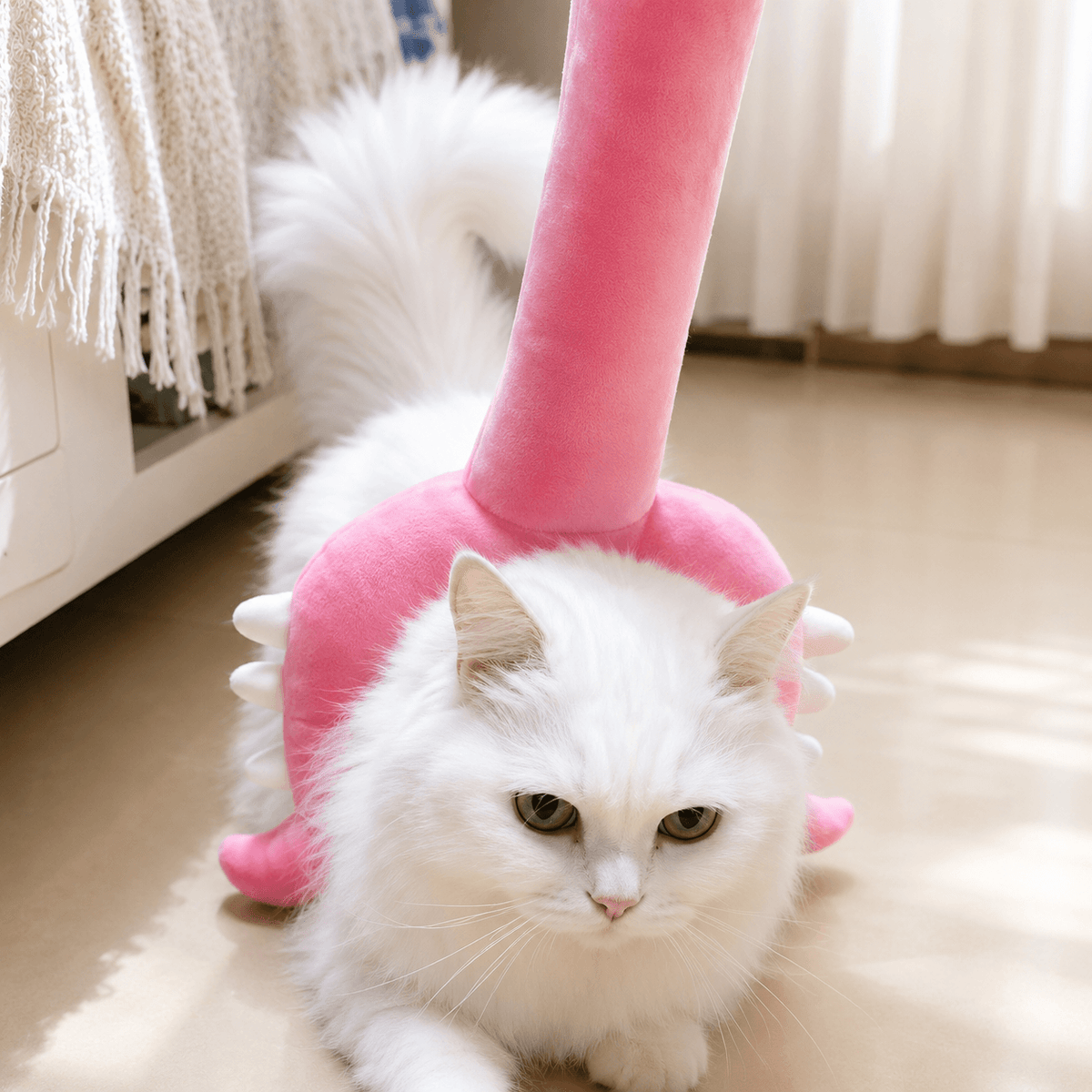 A long haired white cat lying on the floor with the pink plush head curved around its head and shoulders.