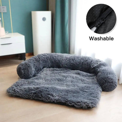Dark gray plush dog couch bed with its U-shaped bolster and washable zip cover, on a wood floor.