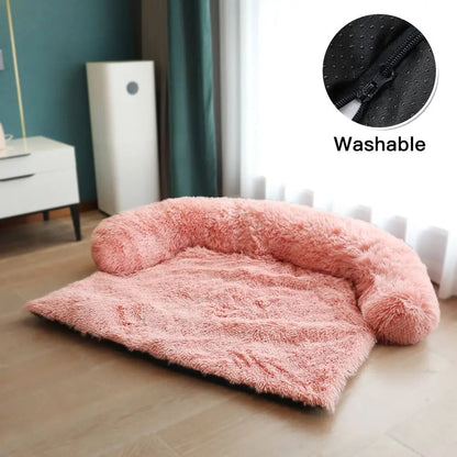 Pink plush dog couch bed with its U-shaped bolster and washable zip cover, on a wood floor.