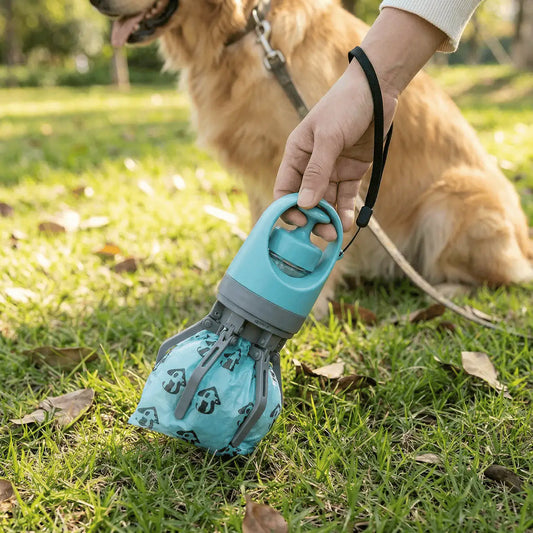 Hand using the teal portable claw pooper scooper with a bag over the claws on grass, a golden retriever behind.