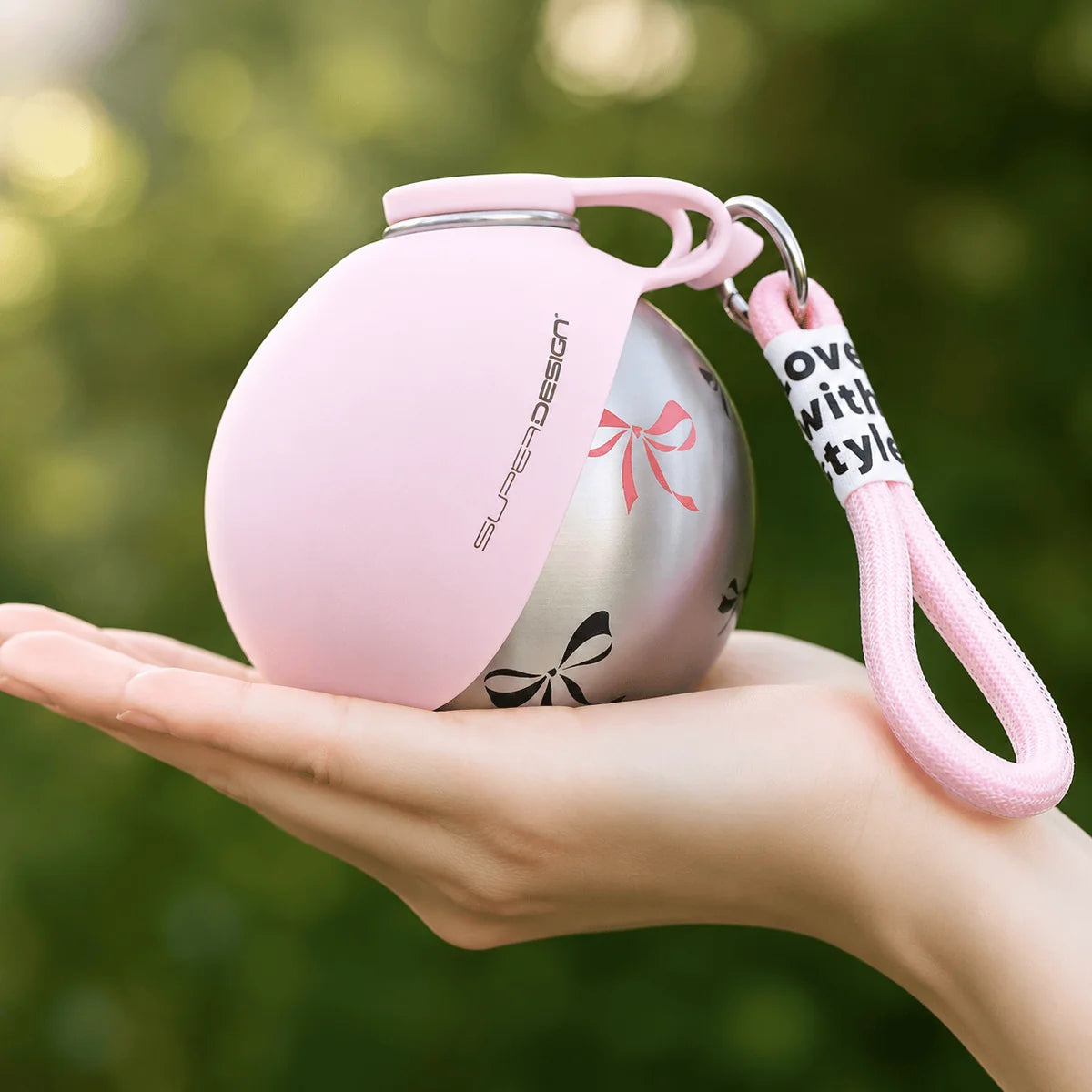 Pink portable dog water bottle with a bow print body and lanyard resting in an open palm.