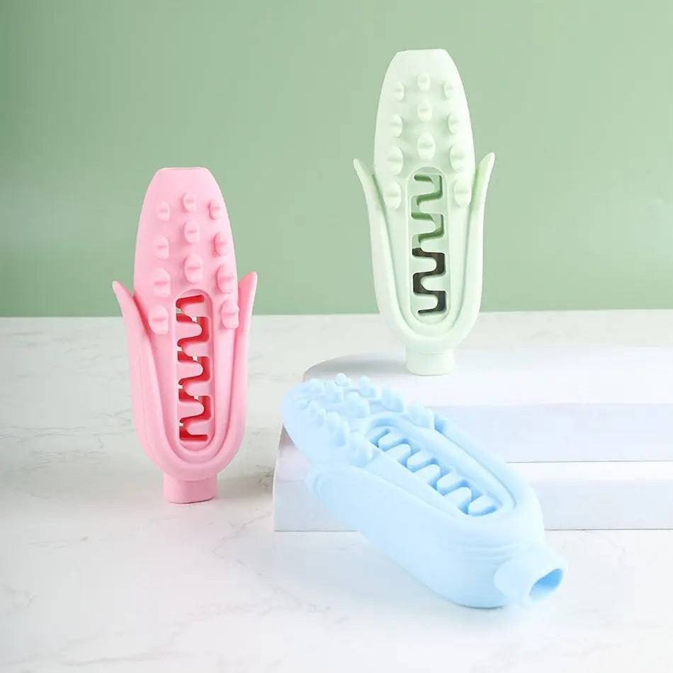 Pink, green and blue silicone corn dog chew toys on a white block against a green wall.