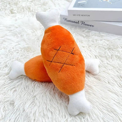 Two orange plush chicken leg squeaky dog toys with white bone ends on a fluffy rug.