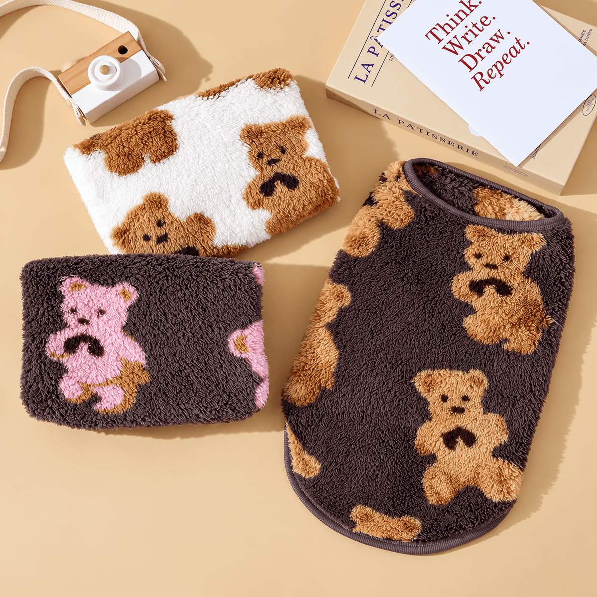 Flat lay of three teddy bear fleece dog vests in white, brown with pink bears and brown with tan bears.