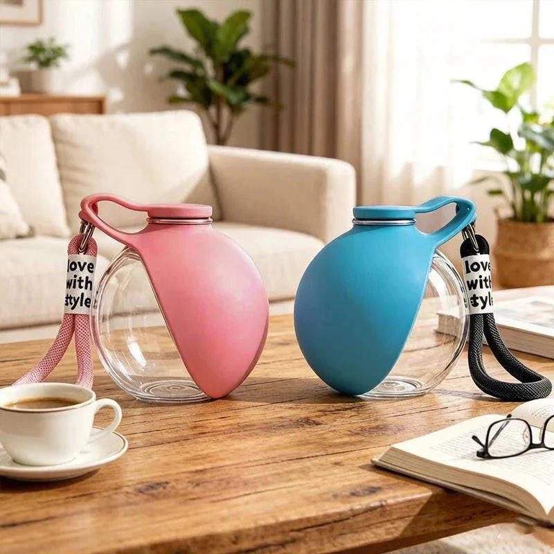 Pink and blue travel dog water bottles on a wooden coffee table beside a cup of coffee and a book.