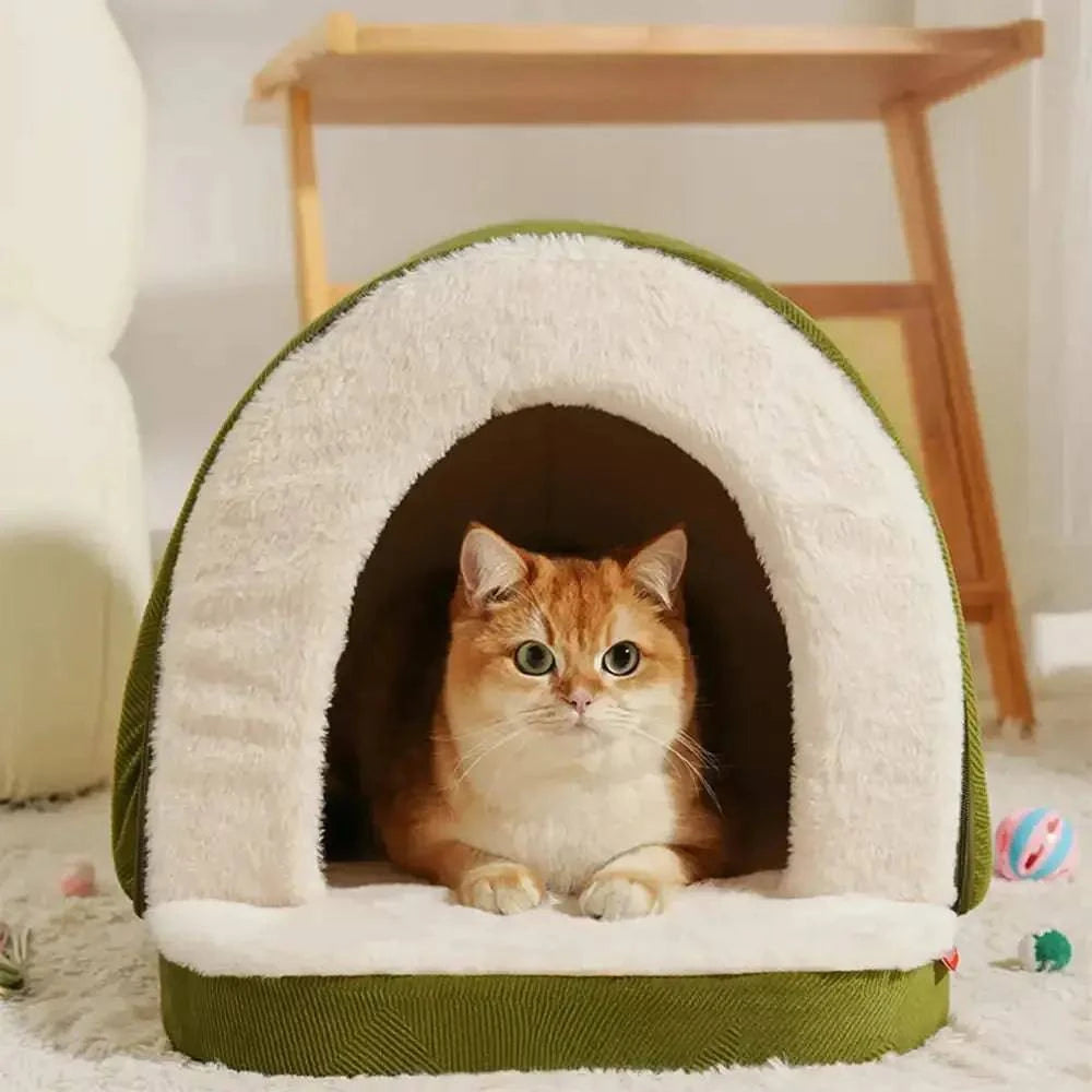 Orange cat resting inside the green cave bed with toys scattered on the rug outside.
